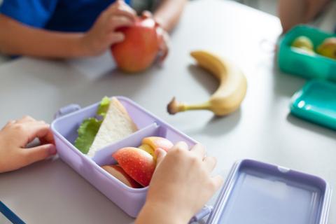 Kids at a school lunch table eating sandwiches and fruit.