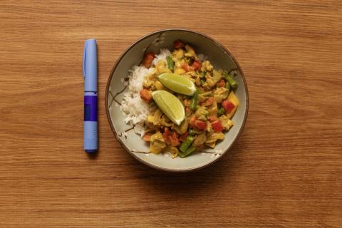 A vial of Ozempic sits on a table next to a bowl of rice and vegetables.