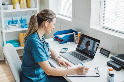 A doctor sits at her desk, talking to another doctor by videoconference.