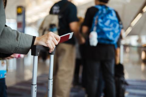 A person pushes a rolling suitcase through an airport while holding a boarding pass.