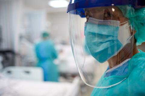 A doctor wearing a gown, mask, and face shield in a busy trauma centre.