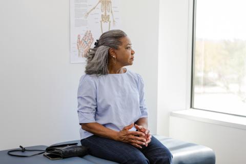 A senior patient sits on an examination table, looking out the window.