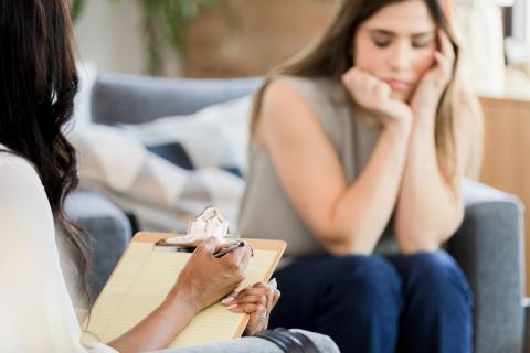 A doctor talks to a worried-looking patient sitting on a couch.