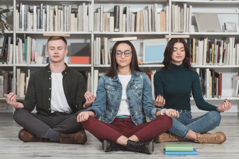 Multicultural students meditating with books on heads in library