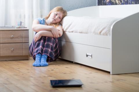 Girl sitting on bedroom floor looking at scale