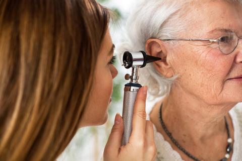Doctor holding otoscope and examining ear of senior woman
