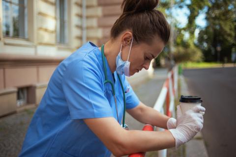 A doctor stands outside of a hospital, leaning on a railing and looking distressed