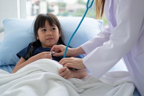 A doctor attends to a child lying in a hospital bed.
