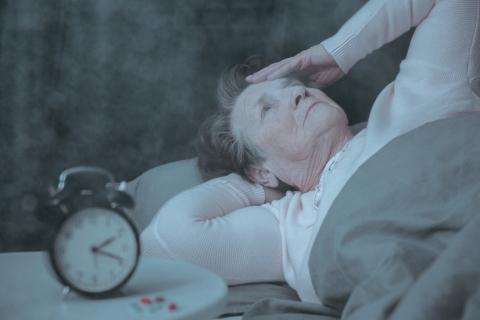 Old woman in bed who has a sleep disorder, alarm clock on the bedside locker