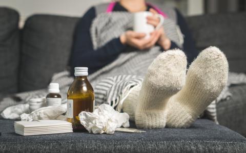 Woman couch ridden battling the flu with cough medicine and tissues