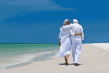 A couple stands on the beach holding hands