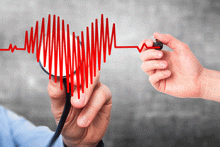 A doctor holds a stethoscope up to an electrocardiogram printout in the shape of a heart