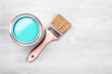 A paintbrush sits beside a can of light blue paint