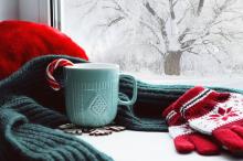 A table by the window with gloves, a scarf, and a mug with a candy cane in it