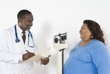 A doctor talks to an overweight patient and writes notes in a folder
