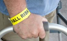 A man with a wristband that reads "fall risk" stands using a walker