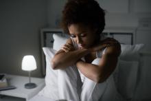 A woman with depression sits in bed with her hands around her knees