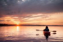 A woman in a kayak faces a sunset.