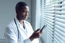 A doctor texting by a window with a serious expression.