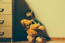 Little boy sitting on floor by dresser hugging a teddy bear and crying