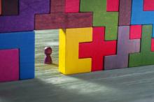 Colourful wall of wooden puzzle pieces with a wooden game piece set in an open rectangle space in the wall