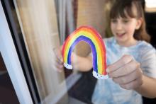A child holds a drawing of a rainbow up to the window