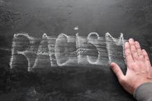 A hand wipes the word "Racism" from a chalkboard