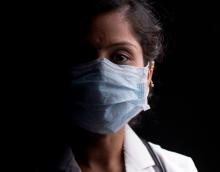 A doctor wearing a mask looks directly into the camera