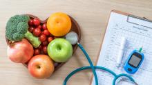 Healthy food arranged in a heart shape, a stethoscope, and diabetes monitoring equipment