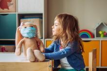 A child plays with a stuffed toy wearing a face mask