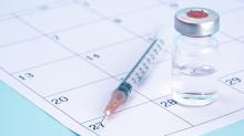 A vial of vaccine and a syringe sit on top of a calendar page