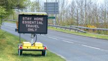 A digital messaging sign on the side of the road with the words "Stay home. Essential travel only"