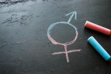 Pink and blue chalk sit next to a chalk drawing of the transgender symbol