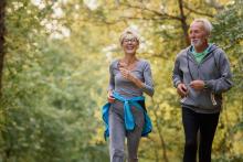 An older couple jogs on a trail surrounded by trees