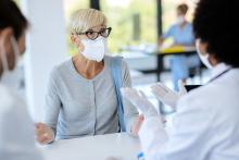 A businessperson wearing a mask talks to two doctors in a hospital