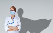 A doctor stands in front a wall; her shadow behind her looks like a superhero