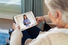 A senior sits on a couch, talking to her doctor on a tablet