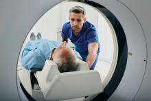 A patient lies on a CT scanning table while a technologist assists