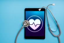 A stethoscope sits on a tablet with a heart shape on the screen