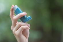 A person is standing outside holding an inhaler to their mouth