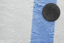 A hockey puck crosses the blue line on an ice rink.