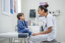 A smiling doctor talks to a young child patient.