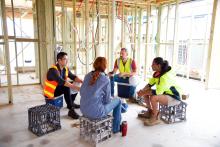 A group of workers wearing high-visibility vests sit on crates, talking.