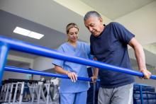 A physiotherapist helps a patient walk using handrails.