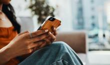 A teenager or young adult sits on a couch, using a mobile phone.