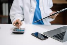 A doctor uses a calculator while working at their computer.