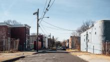 Rundown apartment buildings on either side of a potholed street.