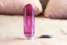 A bottle of lubricant and condoms on a pink bedsheet with two pillows in the background.