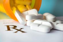 White tablets spill out from a pill bottle onto a prescription notepad.