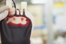 Bag of blood being held up by a medical professional with a blurred background